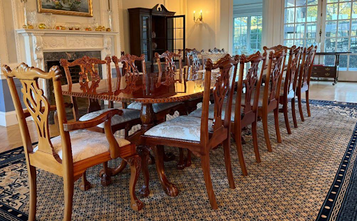 Antique mahogany dining table with ornate carved chairs on a Persian-style rug in a formal dining room, available from Attic to the Basement estate sales.
