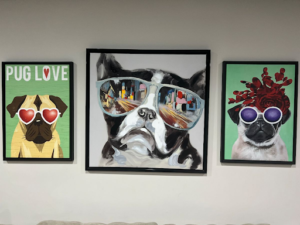 Framed wall art featuring three pug-themed paintings: one with heart-shaped glasses and “Pug Love” text, one close-up pug in reflective sunglasses, and one pug wearing purple sunglasses and a red floral crown.